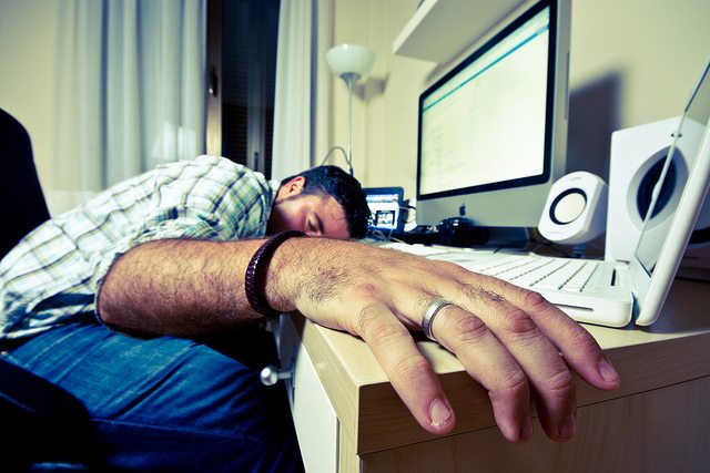 A man sleeps with his face on his computer desk