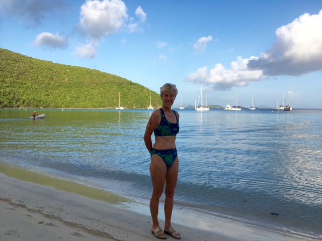 Woman posing for picture on the beach with boats in the background